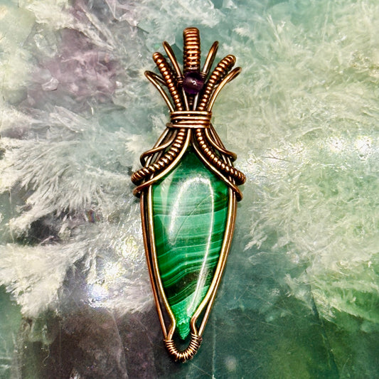Tear shaped malachite stone wrapped in an "art deco" design with copper wire and accented with an amethyst bead