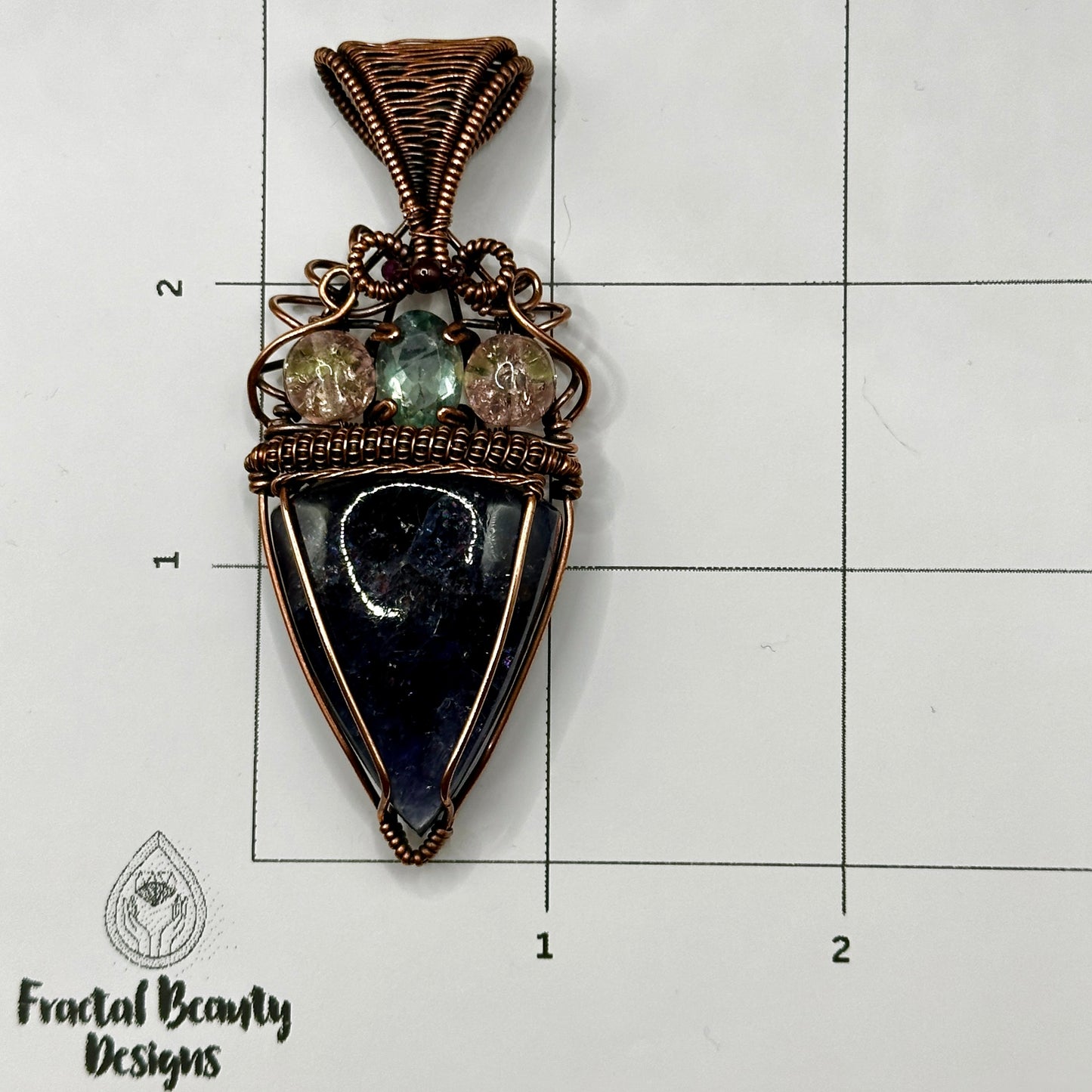 An Iolite Sunstone wrapped in antiuqed copper with 2 Uranium Glass Beads & Fluorite Facet on measuring grid