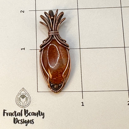 Oval Sunstone wrapped in copper in an "Art deco" design on a measuring grid