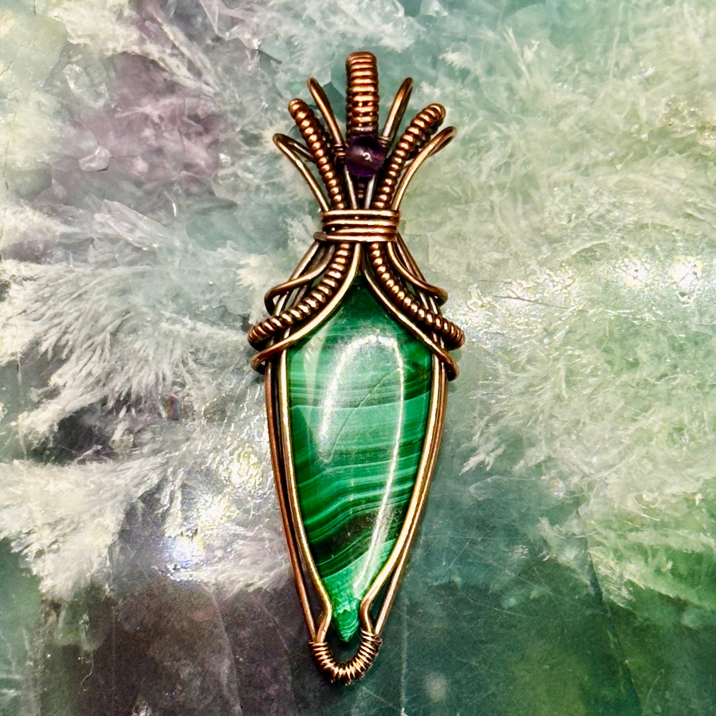 Tear shaped malachite stone wrapped in an "art deco" design with copper wire and accented with an amethyst bead