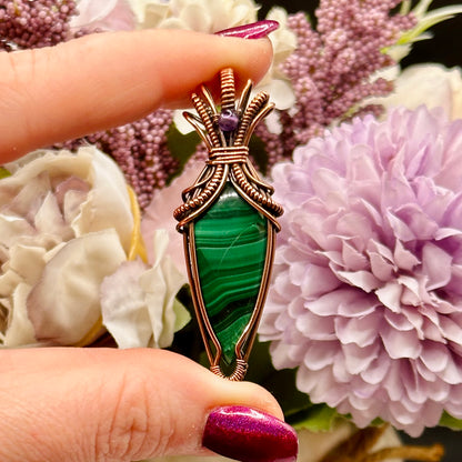 Tear shaped malachite stone wrapped in an "art deco" design with copper wire and accented with an amethyst bead