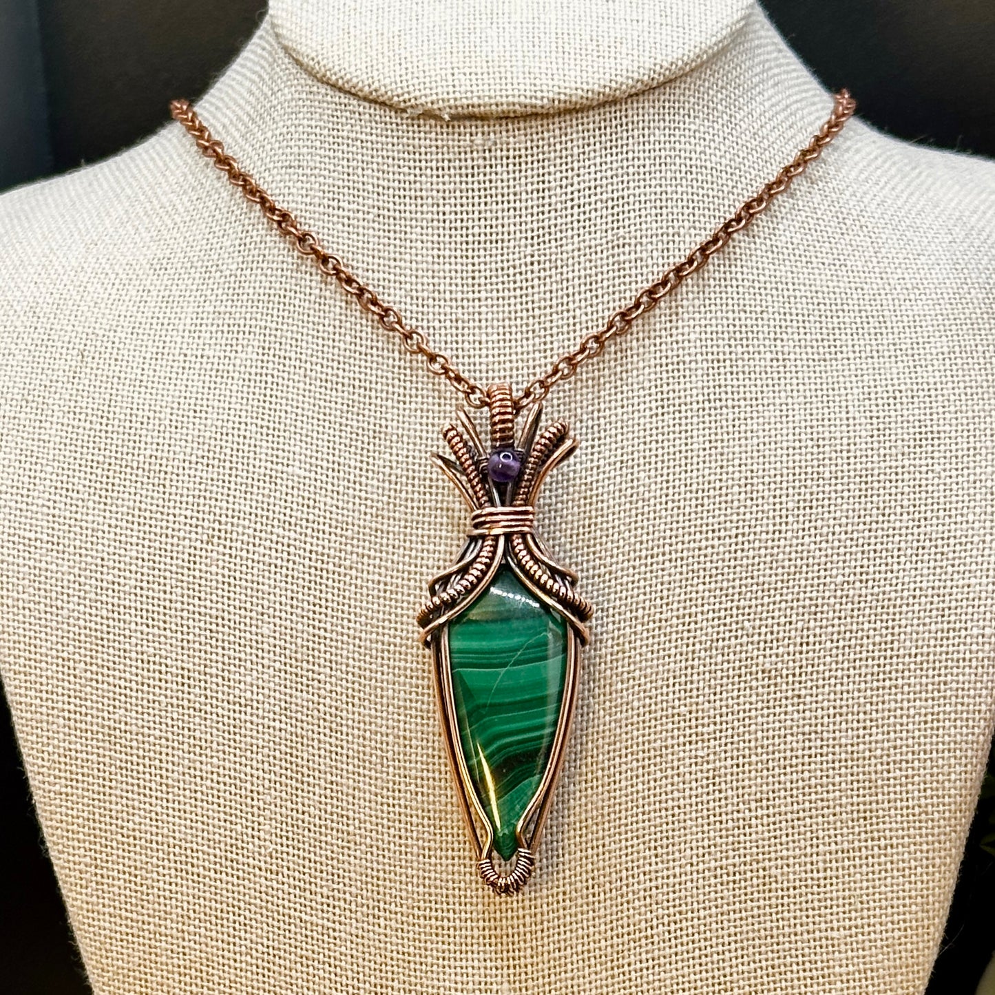 Tear shaped malachite stone wrapped in an "art deco" design with copper wire and accented with an amethyst bead