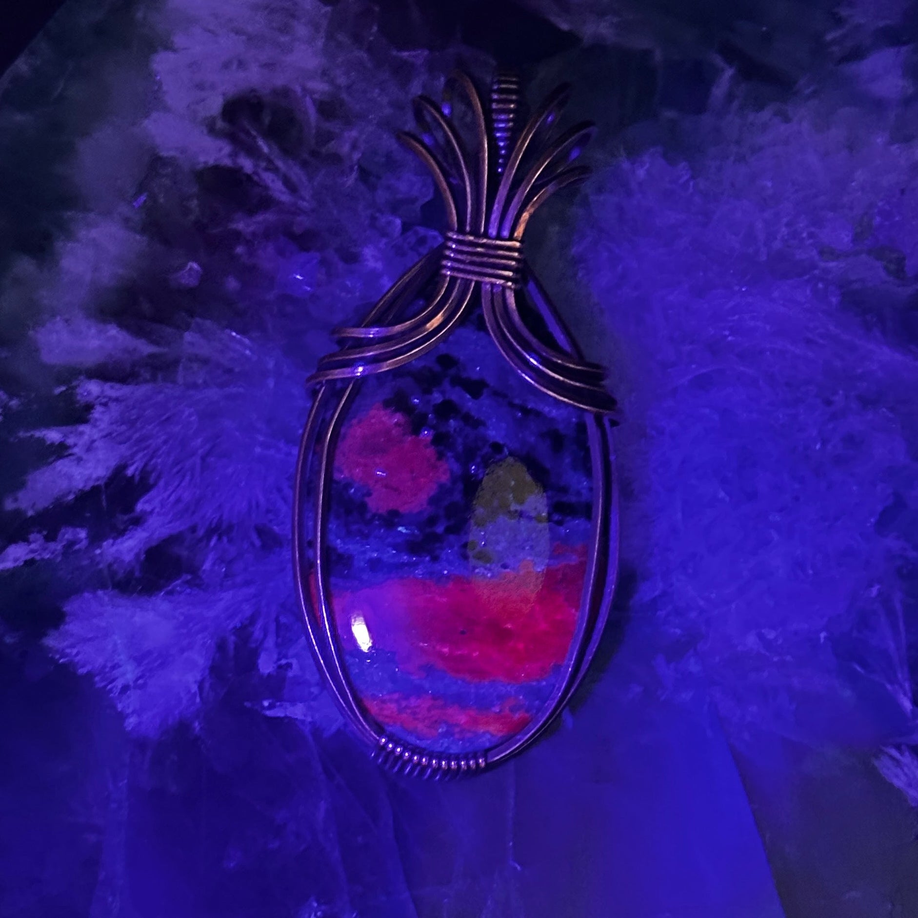 Oval Ruby Zoisite stone wrapped in copper with UV light to show the ruby glow hot pink