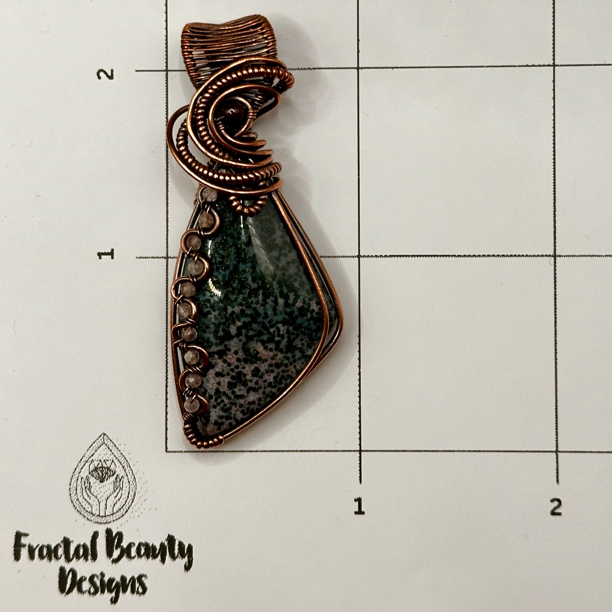 Triangle bloodstone pendant decorated with wavy wire interlaced with rose quartz beads and accented with a garnet bead on measuring grid