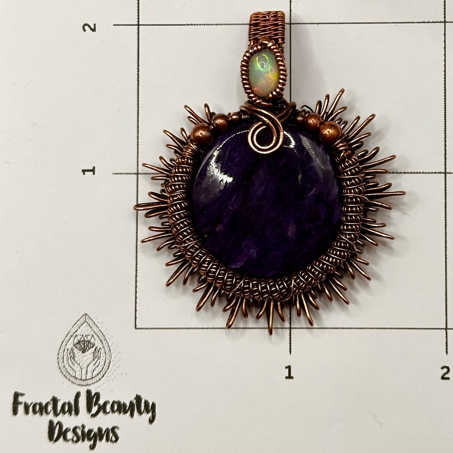 Charoite stone wrapped in sunburst design in antiqued copper accented with a double coil and ethiopian opal on measuring grid