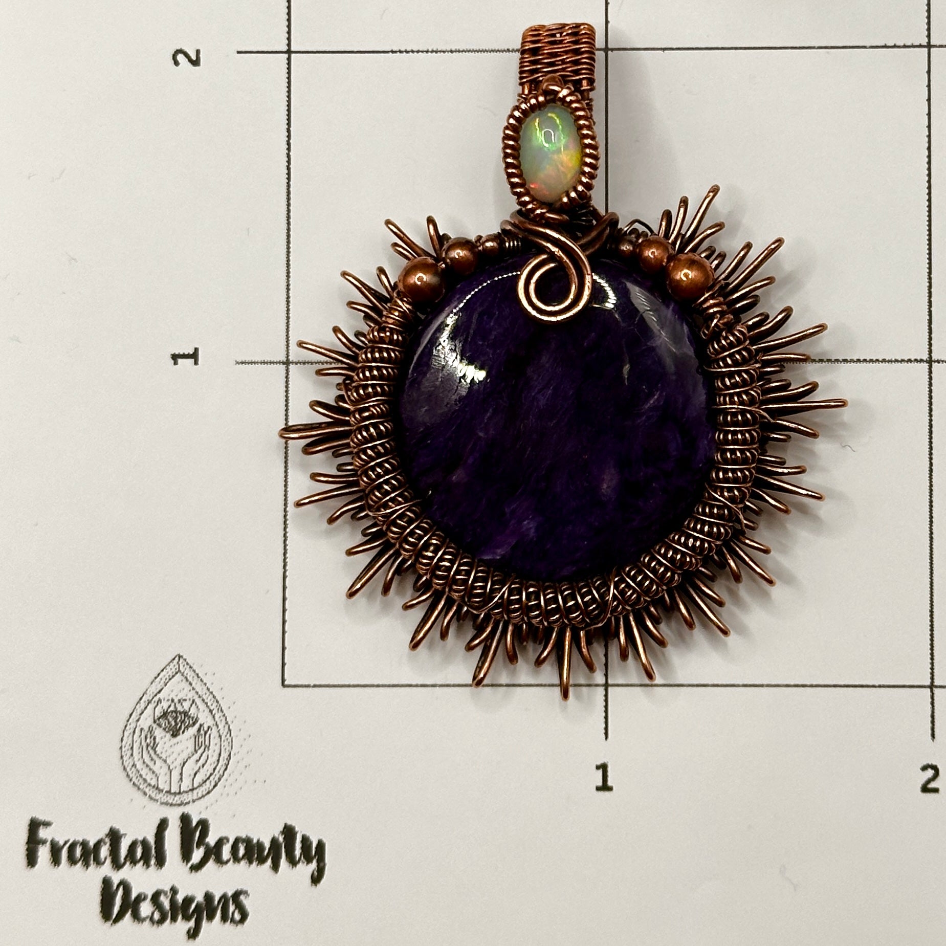 Charoite stone wrapped in sunburst design in antiqued copper accented with a double coil and ethiopian opal on measuring grid