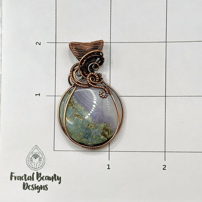 Circular Indonesian Moss Agate stone wrapped in antiqued copper on measurement grid