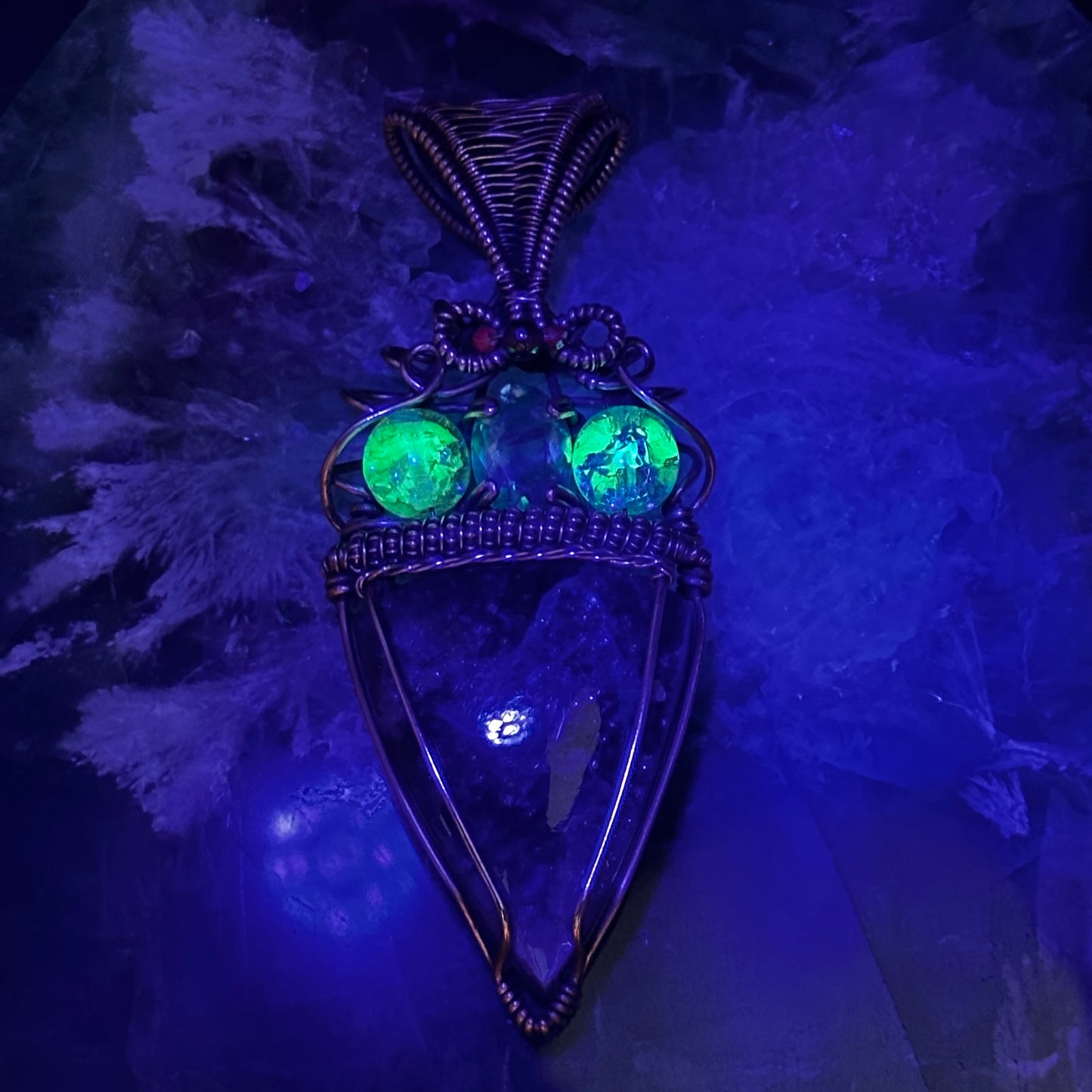 An Iolite Sunstone wrapped in antiuqed copper with 2 Uranium Glass Beads & Fluorite Facet under UV light to show the uranium glow