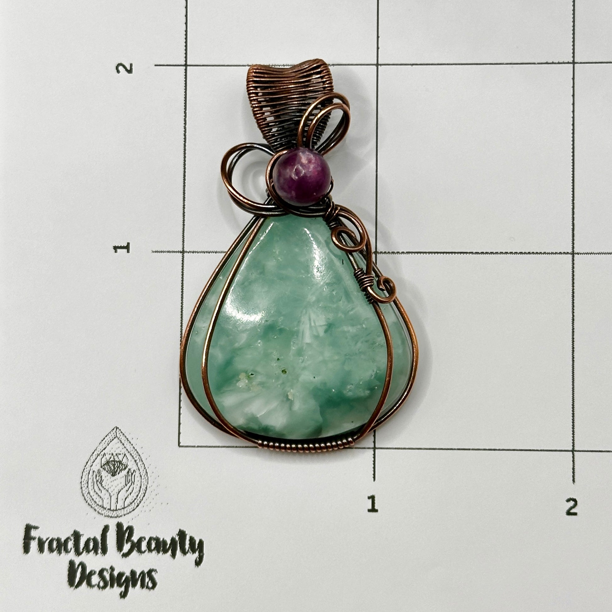 Victoria Stone wrapped in antiqued copper with purple mica bead on measuring grid